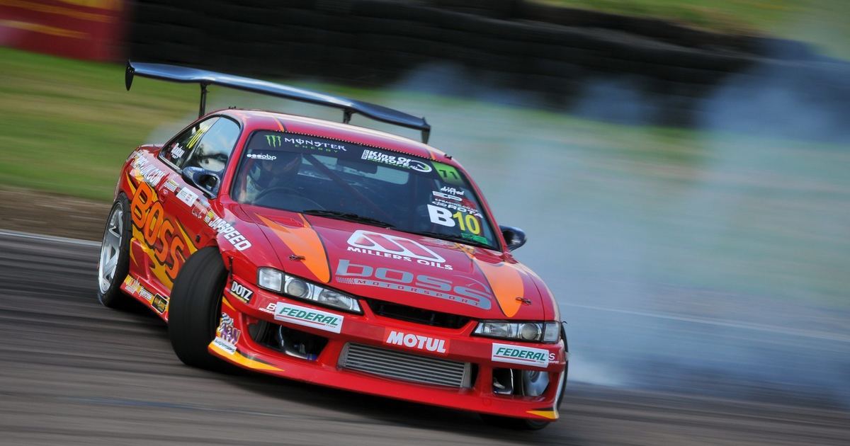 A drift car held sideways under power with tyre smoke