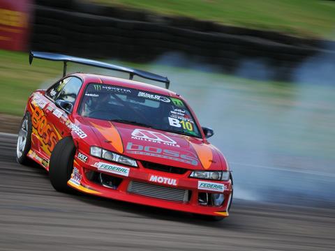A drift car held sideways under power with tyre smoke