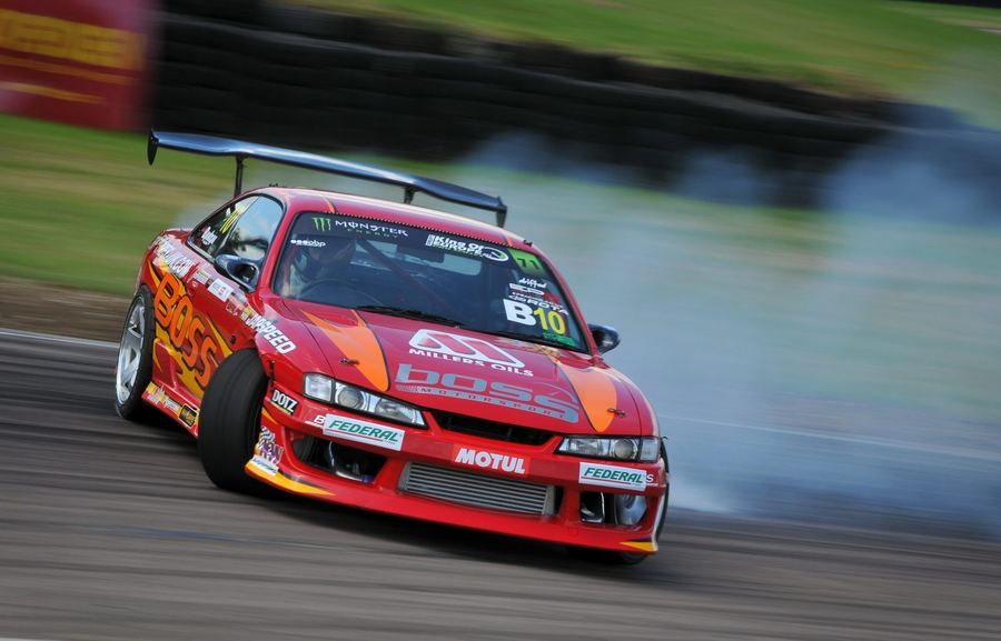 A drift car held sideways under power with tyre smoke