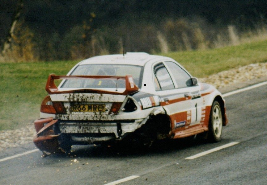 Tommi Mäkinen's Mitsubishi Lancer Evo, missing a rear wheel, still being driven back to service during the 1998 RAC Rally GB — a moment widely remembered as an example of the sport's demands on both car and driver.